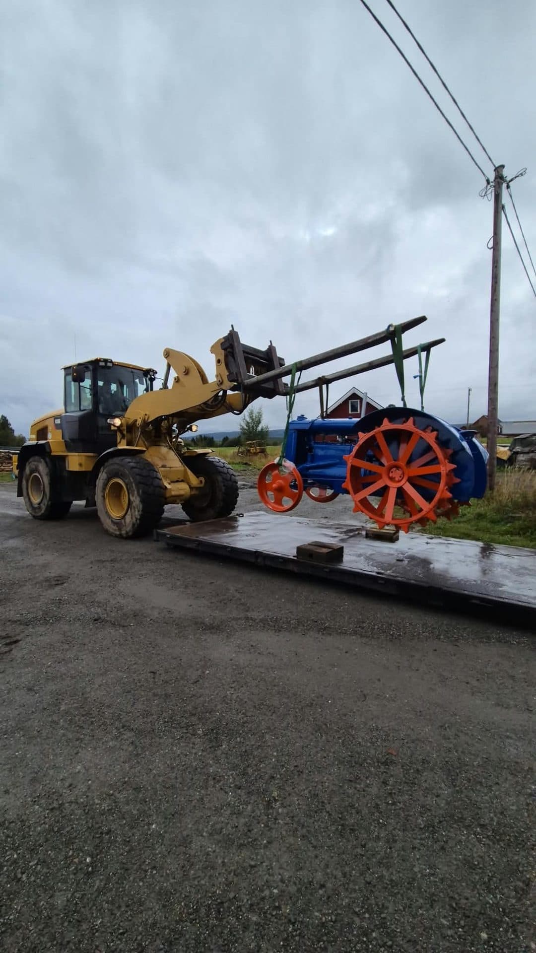 En hjullastare med pallgafflar lyfter en äldre traktor med orange ekerhjul