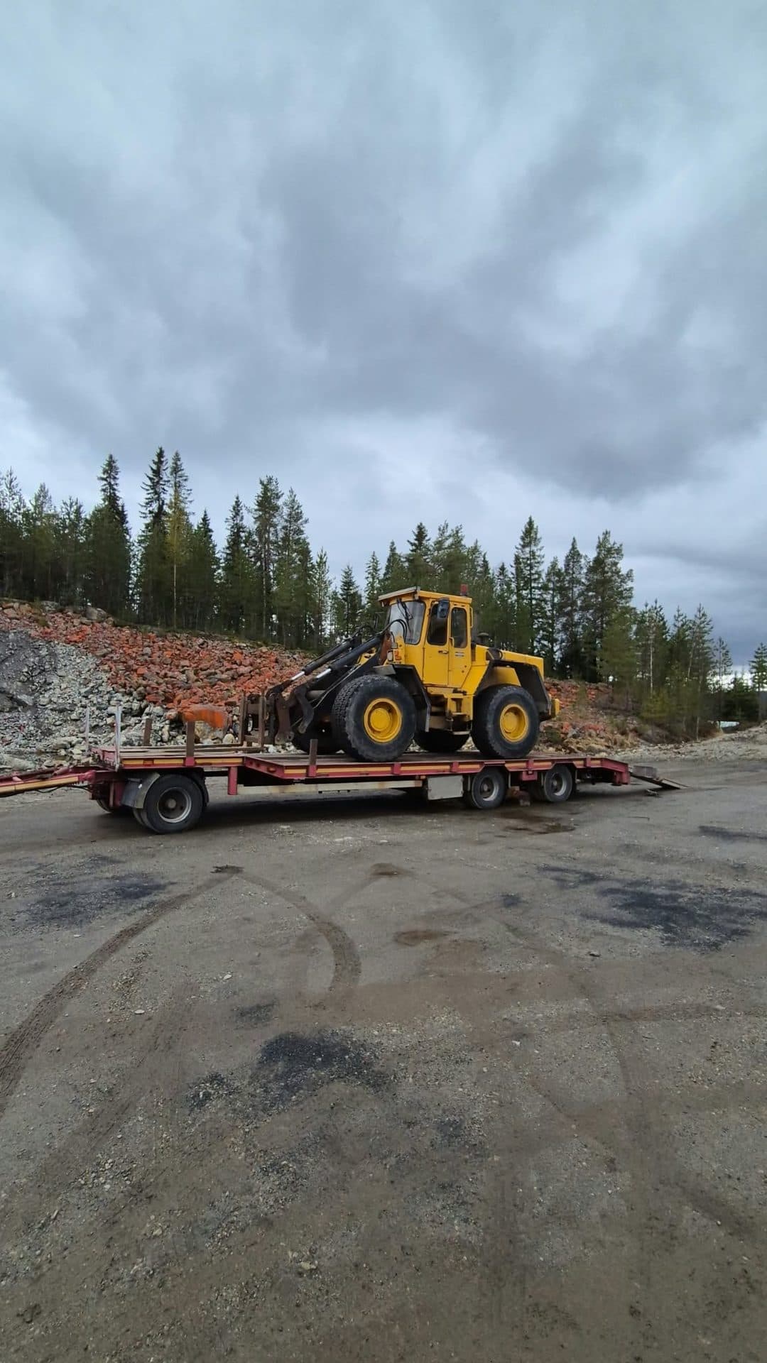 En äldre gul hjullastare på maskinsläpet med ramperna nere, vid ett grustag