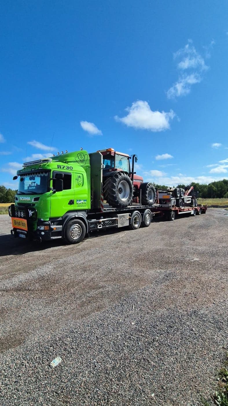 Grön Scania med traktor på flaket och maskinsläp