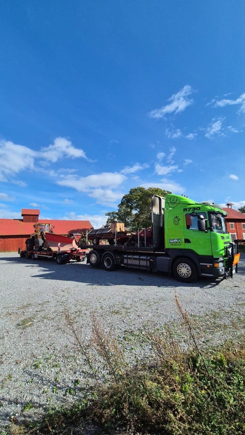 Lastbil och maskinsläp vid en gård med röda hus