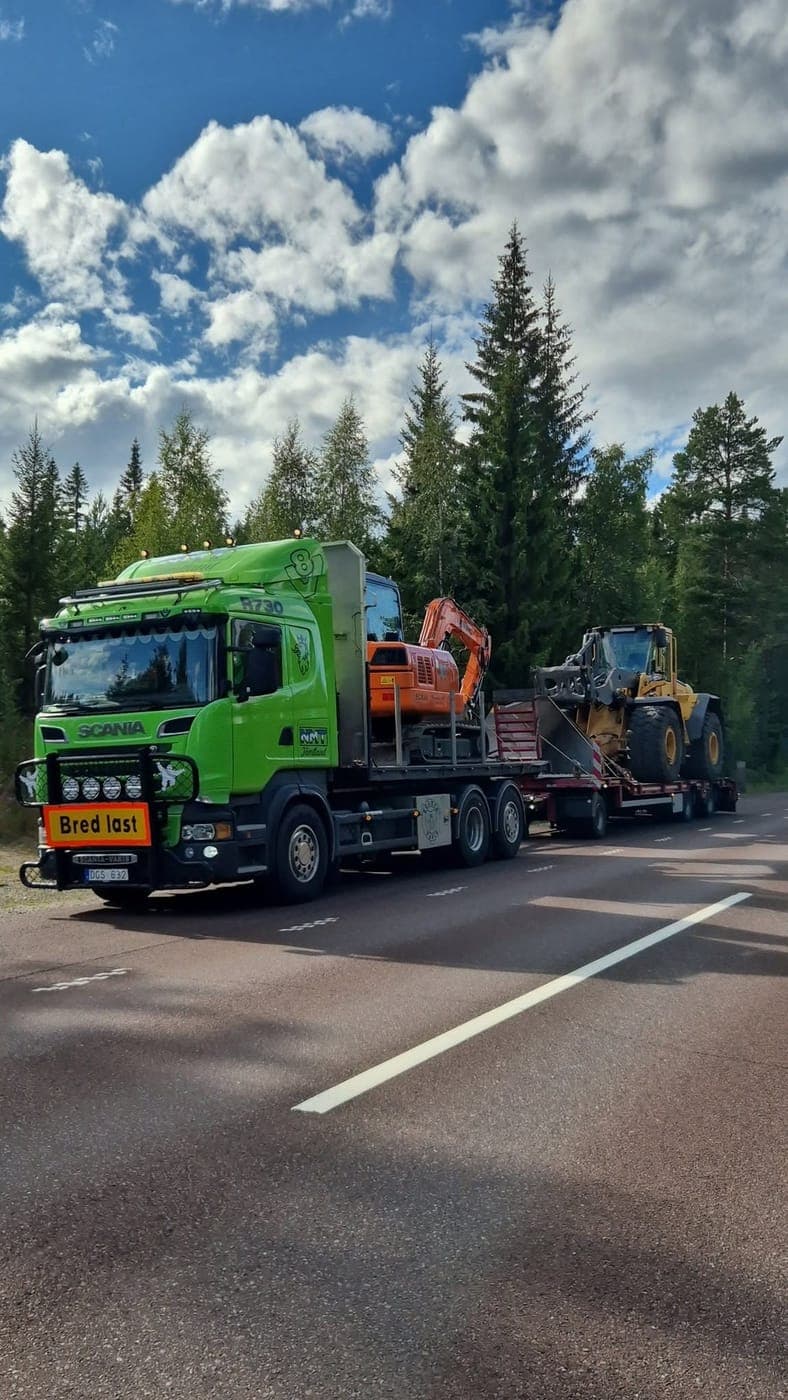 Lastbil med grävmaskin på flaket och hjullastare på släpet, skylt Bred last