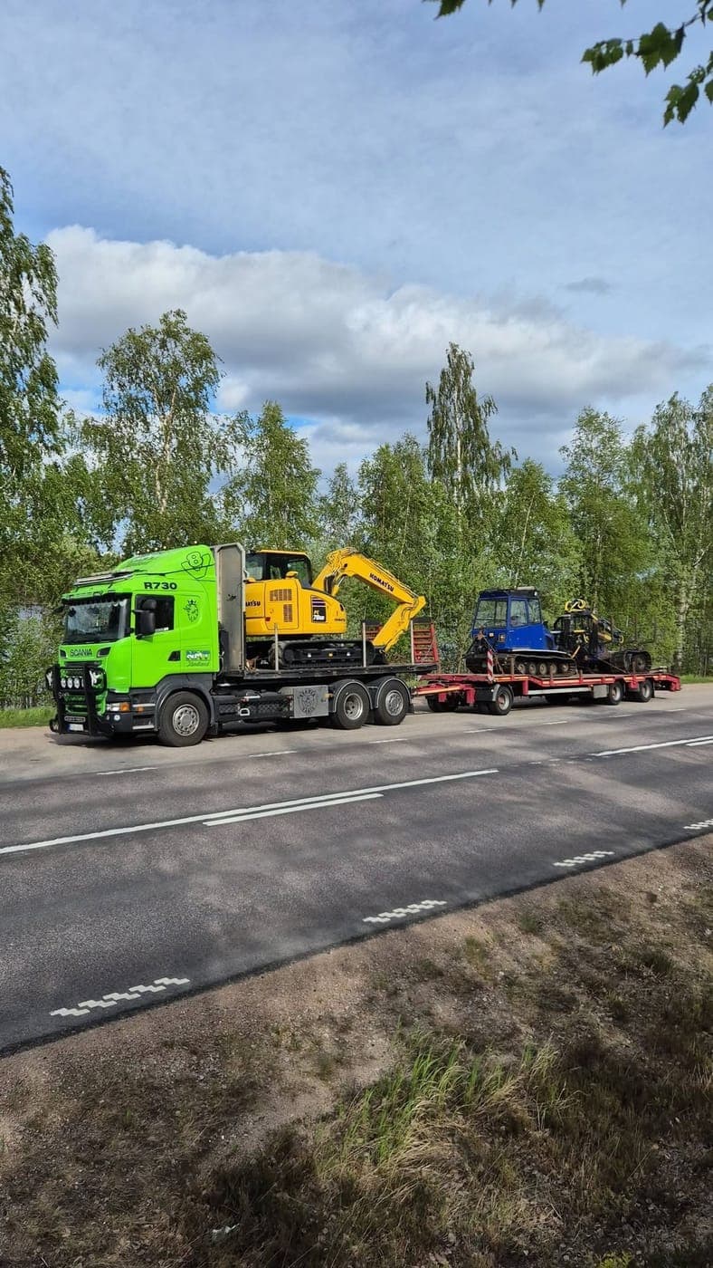 Lastbil med grävmaskin och bandvagn på släpet